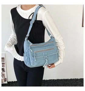 Close-up of light blue denim crossbody bag with multiple zippers and adjustable strap