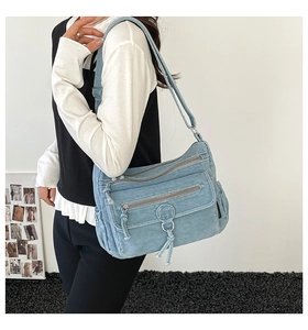 Detail of light blue denim crossbody bag with multiple zippers and fringe zipper pulls