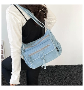 Detail of light blue denim crossbody bag featuring multi-pocket design and silver zippers