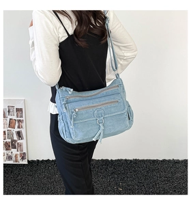 Detail of light blue denim crossbody bag with multiple metal zippers and ring puller
