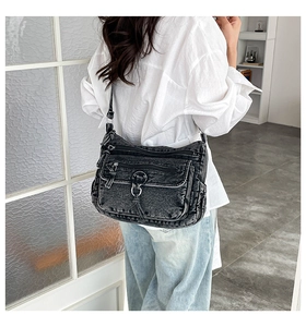 Detail of washed black denim crossbody bag with multiple zip pockets and brand tag