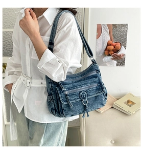 Detail of washed denim crossbody bag featuring multiple zipper pockets and braided drawstring