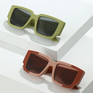 Lunettes de soleil carrées géométriques en vert olive et rouge brique sur socle blanc