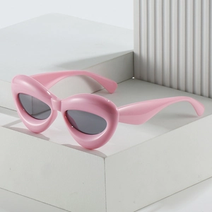 Fashionable pink puffy cat eye sunglasses with dark lenses on a white geometric stand
