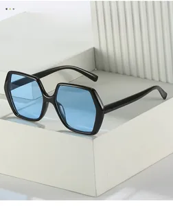 Detail of hexagonal sunglasses with thick black frames and vibrant blue lenses on white stone