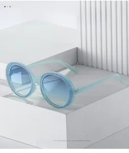 Detailed view of round light blue sunglasses with dark blue glitter trim and gradient lenses