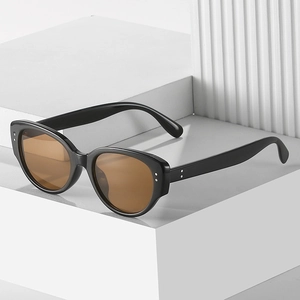 Retro cat-eye sunglasses with black frames, brown lenses, and silver rivets on a block stand