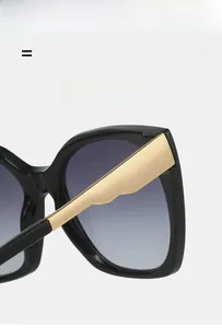 Detail showing square frame sunglasses with gold wavy temples and gradient lenses