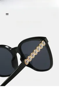 Detail of black cat-eye sunglasses featuring elegant pearl embellishments on the metal temples