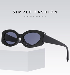 Close-up of stylish black thick-frame sunglasses with dark oval lenses on a white podium