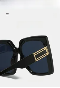 Detail view of square black sunglasses showing the gold metal hinge and elastic frame