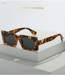Détail de lunettes de soleil écaillées avec logo V doré et clous sur support blanc