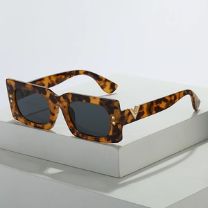 Lunettes de soleil vintage avec détails V dorés et verres gris sur un socle géométrique