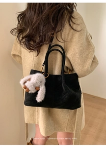 Detail of black suede tote bag with golden rings and a plush bunny charm on a model