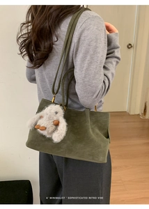 Detail of dark green suede tote bag with plush bunny charm and golden metal hardware