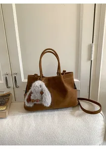 Close-up of brown suede handbag with plush bunny charm and cylindrical dual handles
