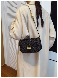 Détail du sac matelassé noir avec chaîne dorée porté par un mannequin en trench