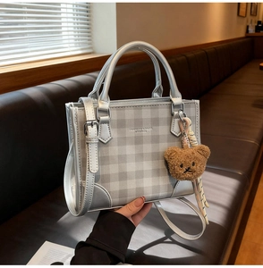 Detail of silver-grey plaid handbag with FASHION & BAGS logo and brown plush bear charm