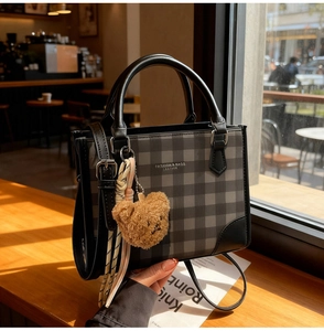 Detail of plaid handbag with leather trim, bear charm and silk scarf in sunlit cafe