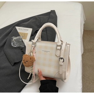 Detail of cream plaid crossbody bag with brown teddy bear charm and twin handles