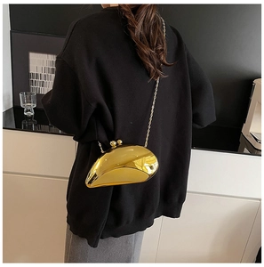 Golden shell-shaped evening bag with metallic finish and thin chain worn by a model