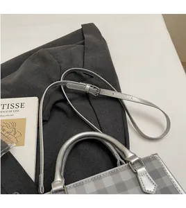 Close-up of grey plaid crossbody bag with adjustable strap on minimalist background