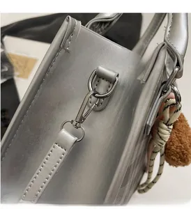 Detail of silver metallic handbag with grid pattern, shiny hardware and plush charm