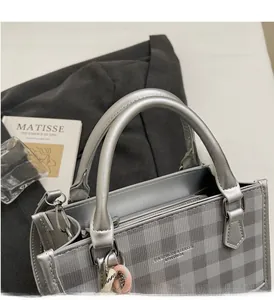 Close-up of a grey plaid handbag featuring a silver round handle and woven ornament