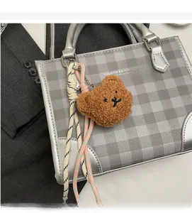 Detail of grey checkered handbag with bear charm and Fashion & Bags text on grey blazer