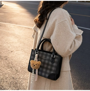 Close-up of black plaid tote bag with brown bear charm worn on a beige wool coat