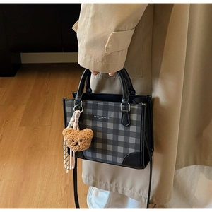 Detail of checkered crossbody bag with brown bear charm held by a model in a trench coat