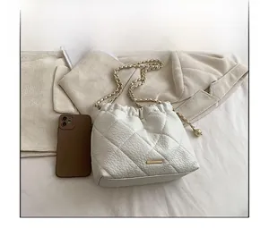 Quilted white bucket bag size comparison with a smartphone and gold chain strap