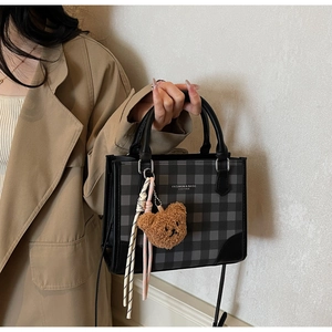 Detail of checkered square handbag with leather handles and cute plush bear charm