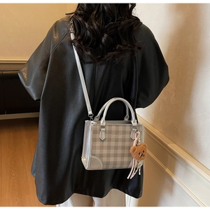 Detail of silver checkered tote bag with plush bear charm worn as a crossbody bag