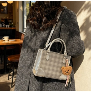 Detail of plaid handbag with plush bear charm in a cozy cafe setting for women