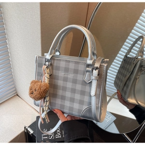 Detail of silver checkered tote bag with plush bear charm and fashion logo text