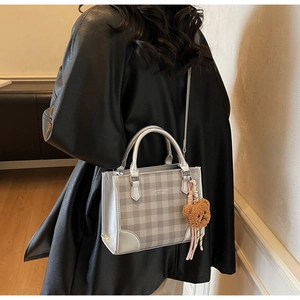 Detail of plaid crossbody bag with silver mirror trim and a plush bear charm on model