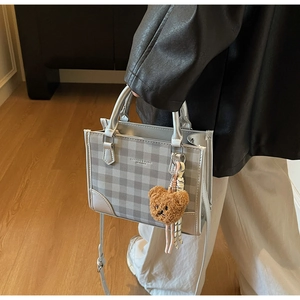 Detail of silver checkered tote bag with fashion lettering and brown plush bear charm