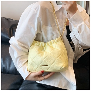 Pale yellow quilted ruched underarm bag featuring a gold chain strap worn by a model