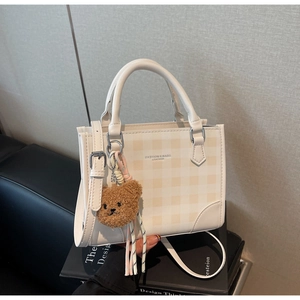 Detail of white plaid crossbody bag with teddy bear charm and fashion leather text
