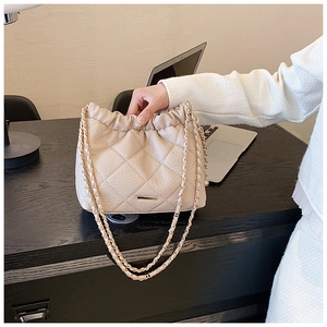 Detail of beige quilted leather bag with drawstring closure and metal chain strap