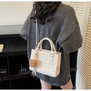 Detail of checkered tote bag with plush bear charm and tassel on a female model