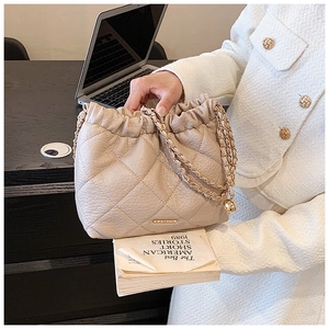 Detail of beige quilted leather chain bag with drawstring closure and golden hardware