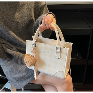 Detail showing white checkered square handbag with a brown plush bear charm accessory