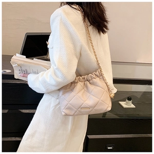 Close-up of beige quilted chain bag with drawstring closure on model in tweed jacket