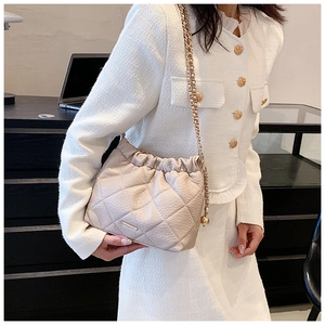 Close-up of cream quilted crossbody bag with gold chain strap on an elegant model