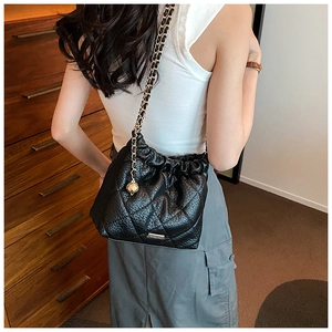 Detail of black quilted chain bag featuring a gold hollow metal ball pendant and strap