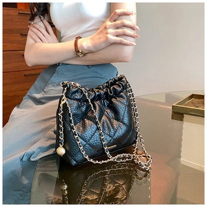 Detail of black quilted leather drawstring bag with gold chain and charm ornament