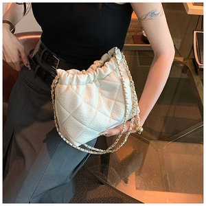 Detail of white quilted drawstring bucket bag with gold chain strap in a lifestyle setting