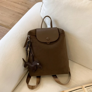 Detail of dark brown canvas backpack with leather flap and cute dachshund charm on sofa